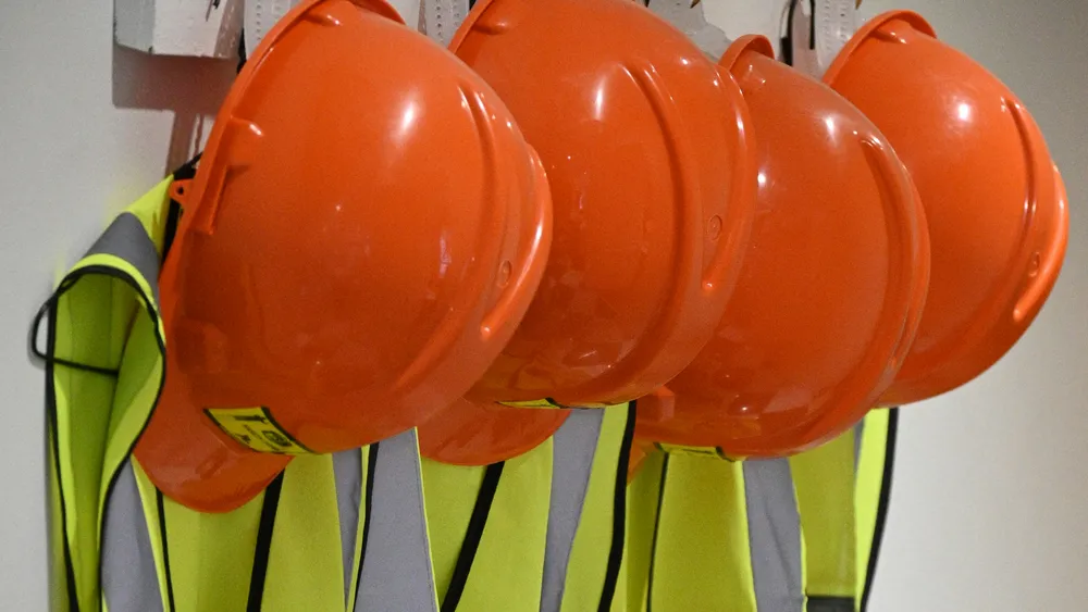 Hard hats and hi-vis vests hanging ready on wall hooks